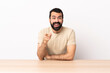 © luismolinero - Caucasian man with beard in a table surprised and pointing front.