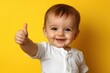 © tonstock - Toddler giving thumbs up smiling joyfully against a yellow background expressing happiness