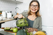 © shurkin_son - Happy cheerful aged female pouring green detox smoothie in glass, having detox nutritious breakfast as antioxidant support to stay healthy and prolong beauty, . Vegetarian diet and weight loss program