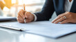 © Tondone - person is signing document with pen, showcasing professional setting with papers and blurred background. image conveys sense of focus and commitment to important tasks