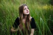 © Довидович Михаил - Blonde woman sitting amid tall grass, gazing skyward with contemplative look, immersed in tranquil natural surroundings