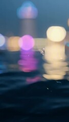 Wall Mural - vertical 9:16 Gentle ripples distort a reflection of city lights on a dark water surface. The colors shift as the water moves, creating an abstract, mesmerizing effect. Dreamy and atmospheric 