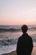 © baby - A person stands at the oceanâ€™s edge, watching the waves wash over the sand. The sky glows softly with the colors of dusk