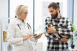 © sofiko14 - Veterinarian presenting treatment details on a tablet to a male owner holding a cat. Setting suggests professional care for pets, demonstrating reassurance and trust between veterinarian and pet owner