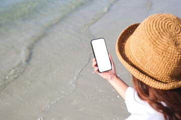 Wall Mural - top view mockup image of a woman holding mobile phone with blank desktop screen by the sea