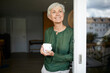 © Westend61 - Senior woman standing with coffee cup by window at home