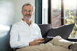 © Westend61 - Senior man with grey hair in modern design living room sitting on couch holding tablet