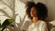 © Anastasia - Young woman sitting on a couch with her eyes closed and her head resting on her hands. she has curly hair that is styled in loose curls and is wearing a white t-shirt.
