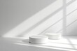 © Ikram - Two simple, white, round podiums.  Natural lighting casts shadows