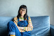 © Davor - Portrait of a happy Asian woman wearing overalls sitting on couch and smiling at home
