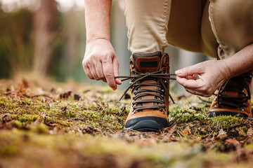 Wall Mural - woman tying shoelace on her hiking boot. tourist is getting ready for hike on trekking trail in fore