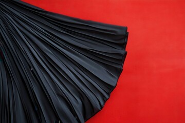 Poster - Elegant black pleated fabric draped against a vibrant red background creates a striking visual contrast for fashion design