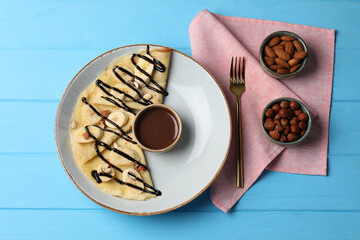 Wall Mural - delicious crepes with banana, nuts and chocolate sauce on light blue wooden table, flat lay