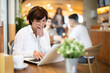 © JackF - Mature woman cafe visitor sits at table with laptop, reads incoming emails and drinks strong coffee. Client is preparing for important meeting, reading text content of report