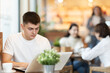 © JackF - Young man is sitting at a table in a cafe and working at a laptop. Guy designer works remotely in a coffee shop