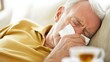 © decle - Nasal congestion in a senior man resting on a couch with tissues and tea. Featuring comfort and relief