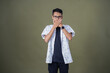 © Nasrul Ma Arif - Young Asian man with casual glasses showing surprised expression, covering his mouth with his hand. Isolated on army green background.