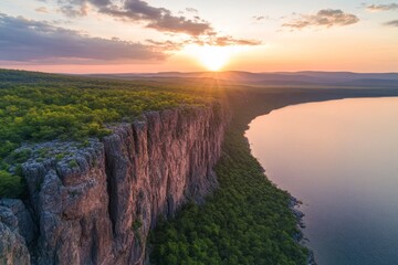 Poster - A towering sandstone cliff rises above a tranquil body of water, illuminated by golden sunlight and creating a dramatic landscape at sunset