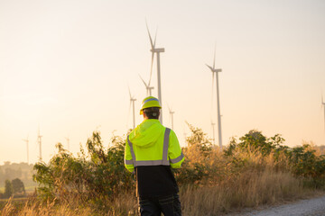 Fototapete - Engineer man working with tablet at windmill farm Generating electricity clean energy. Wind turbine farm generator by alternative green energy.