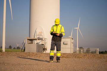 Fototapete - Engineer man working with tablet at windmill farm Generating electricity clean energy. Wind turbine farm generator by alternative green energy.