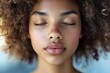© whitestorm - Close-up portrait of a serene woman with closed eyes, showcasing smooth skin and natural curly hair, highlighting beauty, tranquility and peacefulness in a soft light setting.