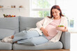 © Pixel-Shot - Young pregnant woman with fresh vegetable salad lying on sofa at home