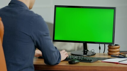 Young Man Working on Desktop Computer with Green Screen Mock Up Display in Modern Home Office. Male Manager With Short Hair Wearing Shirt