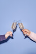 © Seventyfour - Two hands clinking champagne glasses in celebration against plain blue background Creating festive, joyful atmosphere with clear, detailed composition
