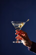 © Seventyfour - Hand holding martini glass garnished with olives against a blue background creating an elegant and sophisticated composition