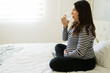© AntonioDiaz - Pregnant woman sitting on bed, sipping water, embodying wellness and hydration during prenatal journey