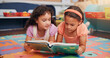 © Jess B/peopleimages.com - Girls, reading book and friends on ground, school and learning with education, growth and literacy knowledge. Group, storytelling and kids in classroom, child development and children with break