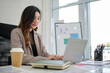 © wattana - Young woman in a business suit is engaged in her work at a well-lit office desk.