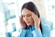 © deagreez - Young professional woman at work experiencing stress or headache in a modern office environment