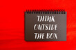 © Emre Akkoyun - Think outside the box message written on black notebook page on red background. Conceptual think outside the box symbol. Copy space.