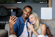 © Wavebreak Media - Celebrating engagement, happy diverse couple video calling with smartphone on couch