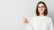 © Sergio IQstock - Happy young woman in glasses and a white sweater pointing to the left, smiling warmly. Concept of promotional banner and friendly approach. young woman, eyeglasses, white sweater,