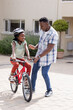 © Wavebreak Media - African American father teaching daughter to ride bicycle, both smiling outdoors