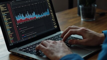 Close-up of hands typing on a laptop with stock market data charts on screen, at desk