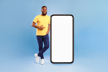 Wall Mural - positive african american guy pointing at big smartphone with mockup for mobile app, recommending co