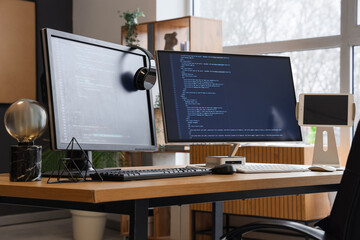 Wall Mural - computer monitors with programming code and headphones on desk in office