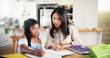 © Malik/peopleimages.com - Mother, girl and homework with book on table for learning assessment, knowledge and support in education. Happy, family and woman with child in house for development, homeschool or help with studying