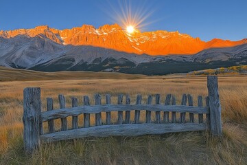 Poster - Sun rises over mountain peaks illuminating grassland at dawn near a wooden fence