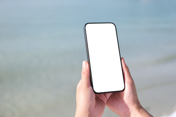 Wall Mural - mockup image of a woman holding mobile phone with blank desktop screen by the sea