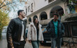 © qunica.com - A group of three young friends enjoying a walk and relaxed conversation outdoors in a charming urban setting surrounded by nature and vehicles, conveying friendship and cheerful outdoor interaction.