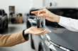 © Vladislav - A close-up of the customer receiving the car keys from the dealer in a showroom. Concept an effortless car buying experience, highlighting professionalism and satisfaction in a luxury dealership.