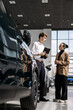 © wedmoments.stock - A car dealer in a modern car dealership advises a customer on buying or leasing a new car. The concept of an expensive purchase or lease of a modern car.