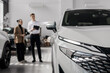 © Vladislav - A car dealer in a modern car dealership advises a customer on buying or leasing a new car. The concept of an expensive purchase or lease of a modern car.