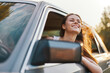© SHOTPRIME STUDIO - Young woman enjoying a road trip, smiling with her hair flowing in the wind from the car window, surrounded by nature in a bright and cheerful setting.