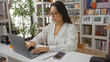 © Krakenimages.com - Young asian woman working on a laptop in a stylish home decor store, surrounded by interior decorations, plants, and shelves filled with books and ornaments.