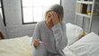 © Krakenimages.com - Woman sitting in bedroom holding pregnancy test looking worried with hand on forehead expressing concern in cozy home environment
